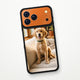 Kozmik turuncu iPhone 17 Pro Max üzerinde siyah çerçeveli MagSafe Frame Kılıf; şeffaf arka panele golden retriever yavrusu fotoğrafı basılmış, arkadan görünüm.